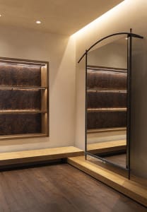 A modern bathroom with a large mirror, wooden floor, and dim lighting, featuring a bench and shower