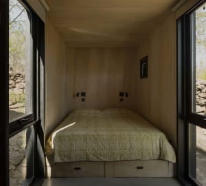 A small bedroom with a bed near a window, allowing natural light to enter, and a door for access to the rest of the space