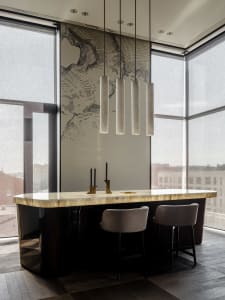 Modern kitchen with a large island featuring a marble countertop, two chairs, and a hanging light fixture, set in a well-lit space with a contemporary design