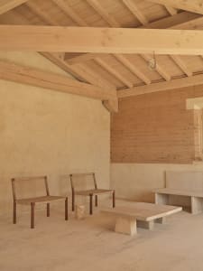 Dining area with a stone wall, wooden floor, and natural light, featuring a stone bench and table, and a dining table with chairs