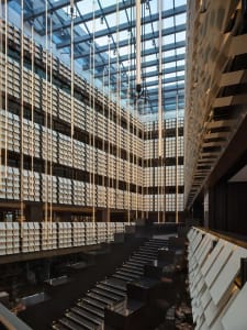 Large modern office building with a glass facade, open interior, and a metal staircase, lit by natural sunlight