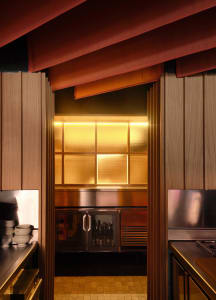 A dimly lit kitchen with a counter and refrigerator, featuring a few bottles on the counter
