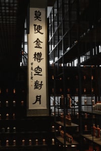 A dimly lit indoor building with a modern aesthetic, featuring a large white sign with foreign text and scattered bottles, set against a predominantly dark background