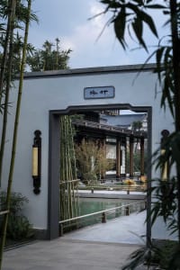 A traditional building with a large entrance featuring bamboo elements, set in an outdoor environment with a nearby pond