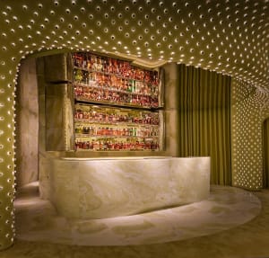 A dimly lit bar with a marble bar and a visually appealing display of liquor bottles