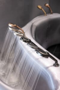 A modern bathroom with a metal sink and brass shower head, featuring dim lighting and a moody atmosphere