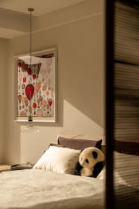 A dimly lit bedroom with a bed, a stuffed panda bear, and a picture on the wall