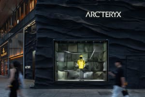 A dimly lit storefront with a stone exterior, featuring a display window with a mannequin wearing a yellow jacket and showcasing various items