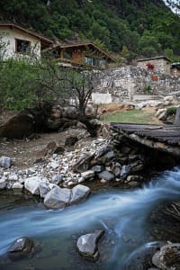 A rustic house with a wooden bridge crossing a stream in a natural environment