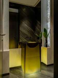 Bathroom with a glass sink, mirror, and potted plant in a dimly lit space with a black and white color scheme