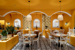 Warm and inviting restaurant with a yellow color scheme, featuring a dining area with tables and chairs, a bar area, and cozy ambiance