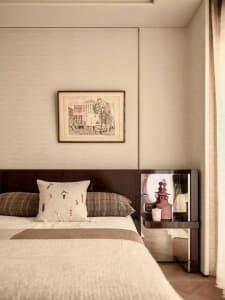 Cozy bedroom with a bed covered in a white blanket, a wooden headboard, and a picture frame on the wall, with a table and lamp nearby