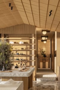 A dimly lit room with wooden walls and floor, featuring a dining table, chairs, vases, bowls, and a potted plant, creating a cozy and intimate atmosphere