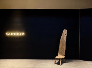 A modern living space with a wooden chair in front of a black wall, on a wooden floor, with a calm and inviting atmosphere