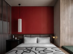 Cozy bedroom with a modern bed, black nightstand, and white lamp, set against a backdrop of warm red walls