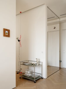 A calm and inviting living space with a white wall, metal shelf, glass clock, and red wire, lit by natural sunlight