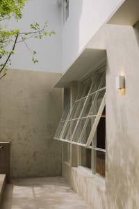 A stone building with an open window and closed door, set in a serene courtyard with a tree in the background