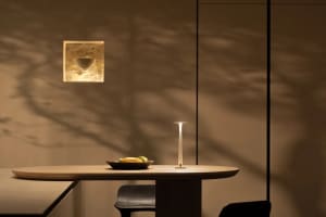 A dining area with a wooden table and chairs, set with a bowl of fruit, lit by a table lamp