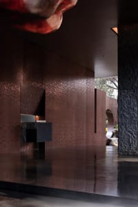 A dimly lit bathroom with a brown and red color scheme, featuring a black counter, brown tiles, and a mirror on the wall