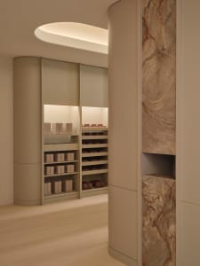 Bathroom with a marble wall and counter, featuring multiple bottles of various sizes on the counter in a dimly lit, luxurious space
