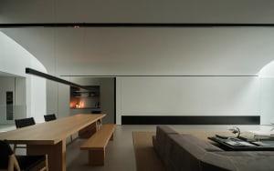 A well-lit living room and kitchen with a couch, chair, coffee table, dining table, counter, and decorative items, featuring wood and glass materials