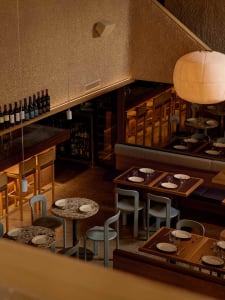 Cozy restaurant interior with wooden floor, dining tables, chairs, and wine bottles, dim lighting creates an intimate ambiance