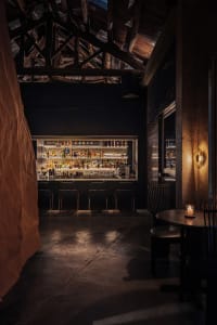 A dimly lit bar with a black and white color scheme, featuring a display of liquor bottles, chairs, and a dining table