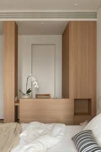 A cozy bedroom with a wooden floor, white walls, a bed, a desk, and a chair, creating a comfortable atmosphere