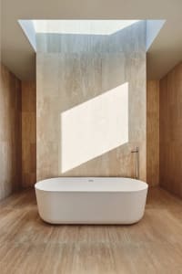 A modern bathroom with a large white bathtub, shower head, and large window for natural light, giving a clean and bright appearance