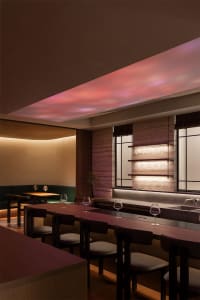 a modern restaurant interior with a long wooden table, chairs, wine glasses, and a potted plant, soft warm lighting