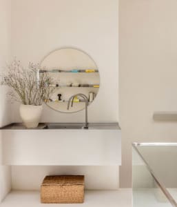 A well-lit bathroom with a sink, mirror, and vase, featuring predominantly white materials