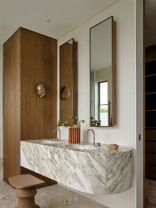 Modern bathroom with a marble countertop, a white sink, and two potted plants, surrounded by a large mirror and soft warm lighting