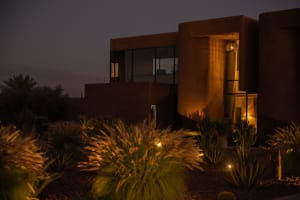 A modern house with a red brick exterior, curved wall, and large window, well-lit at night