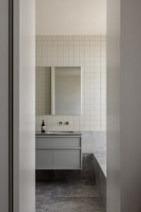 Modern bathroom with a marble sink, tile walls and floor, and a large mirror above the sink, with a cabinet under the sink for storage