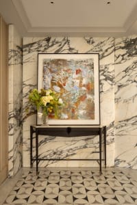 A modern living space with a black frame around a painting of a marble wall, a vase with flowers, and a black bench in the center of the room