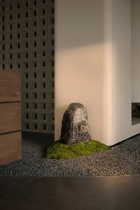 A serene room with a rock on a bed of moss, surrounded by a white wall and a wooden cabinet, on a gravel surface