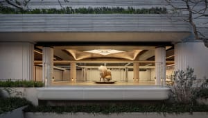 A dimly lit, modern building lobby with a large metal sculpture as the centerpiece, surrounded by concrete walls and floors