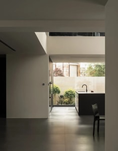 A modern kitchen with a white color scheme, featuring a sink, dining table, and chair, with natural light from a window creating a warm atmosphere