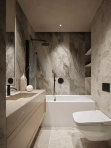Luxurious bathroom with a white bathtub, sink, and toilet, surrounded by marble walls and dim lighting