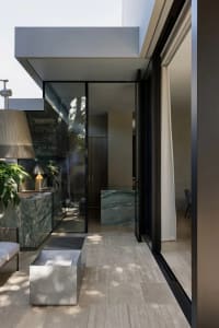 Well-lit bathroom with a large window, marble surfaces, and glass accents, featuring a sink, toilet, and shower