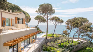 A modern house with a wooden deck and stone features, surrounded by a serene ocean view, with natural light and a bright atmosphere