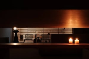 A dimly lit room with a wooden table and chairs, a couch, and a chair, with a candle on the table creating a cozy atmosphere