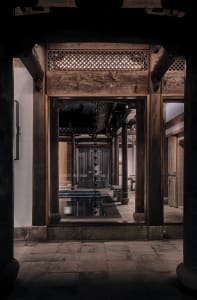 A dimly lit bathroom with a wooden doorway, a bathtub, and an open doorway inviting the viewer in