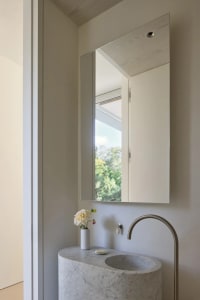 Bathroom with a metal sink, a large mirror, and a vase with flowers on the sink, set in a well-lit space