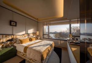 Cozy bedroom with a yellow color scheme, a white and brown blanket-covered bed, and a chair near a window with natural light
