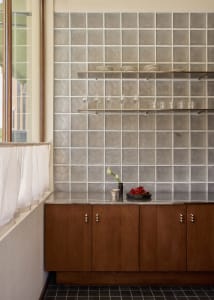 Modern kitchen with a wooden cabinet, tile backsplash, and natural light from a window, featuring wine glasses and a bowl on the countertop