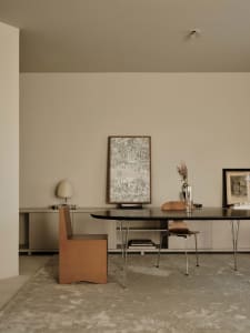A well-lit dining area with a modern wooden table and chairs, a vase on the table, and natural light from a window