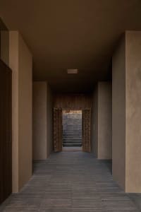 A modern hallway with a doorway, staircase, and ceiling light, featuring concrete and stone materials in a calm and inviting atmosphere