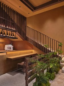 Cozy bar area with a wooden counter, staircase, and seating, dimly lit with a rustic style and warm color palette