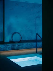 A calm and relaxing outdoor space with a blue tiled pool surrounded by a brick wall and a metal railing